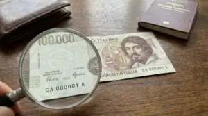 Banconota italiana da 100.000 lire del 1994 osservata con lente d'ingrandimento su tavolo in legno