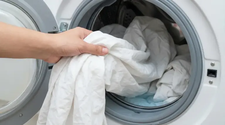 Una mano inserisce lenzuola bianche in una lavatrice a carica frontale