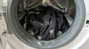 Cestello della lavatrice con bucato scuro e residui di detersivo, segnale di lavaggio che rende i capi duri